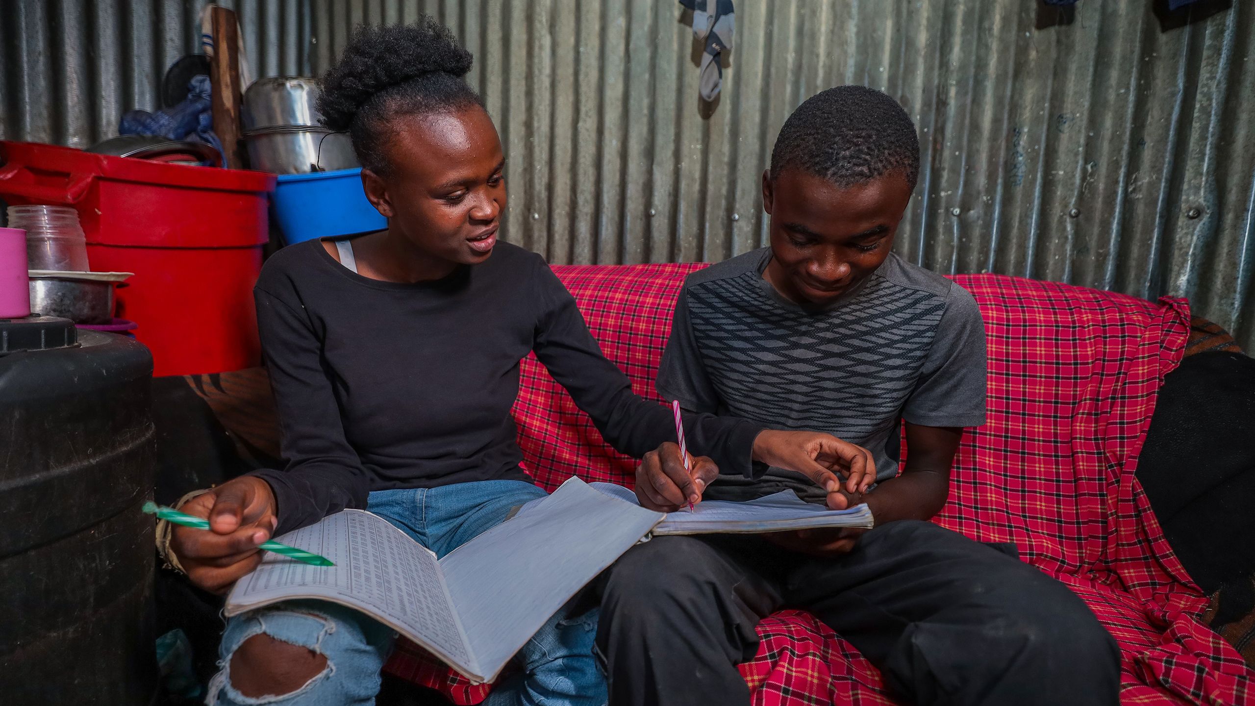 A young woman helps her teenage brother fill out a worksheet as they study together in their home.