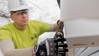 Volunteer in a white hard hat clipping siding on a volunteer build site. 
