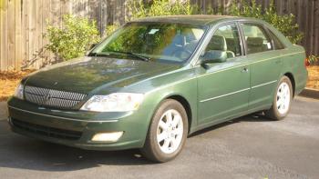 A dark green older model car in a parking space by a fence to suggest vehicle donation.