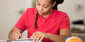 Habitat for Humanity applicant for the affordable homeownership program sits in a red shirt at a desk filling out paperwork.